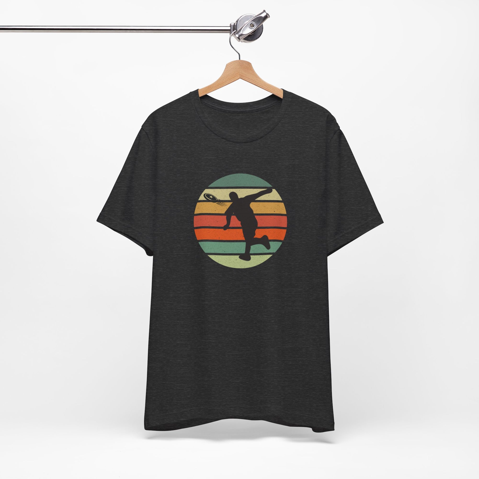Dark gray t-shirt with a graphic of a silhouette disc golf player throwing a disc above a colorful retro graphic, hanging on a wooden hanger.